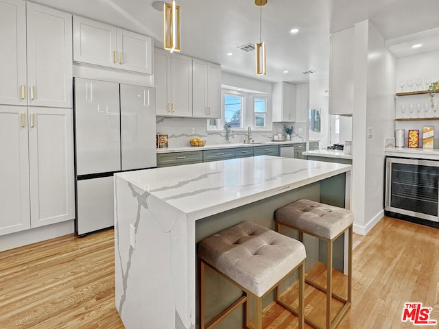 kitchen with white built in refrigerator, beverage cooler, light wood-type flooring, hanging light fixtures, and white cabinets