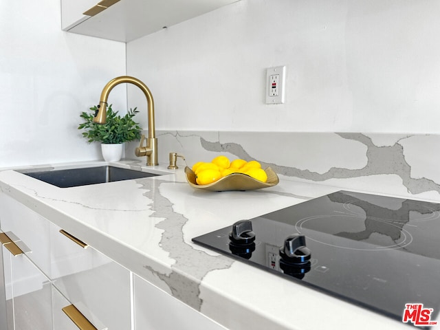 room details featuring sink, white cabinetry, light stone counters, and black electric cooktop