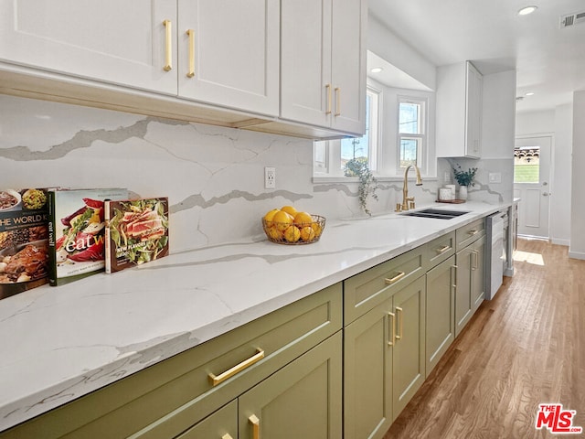 kitchen with light stone countertops, sink, light wood-type flooring, backsplash, and stainless steel dishwasher