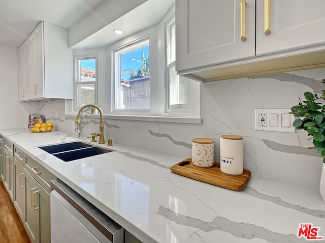 kitchen featuring sink, white cabinetry, dishwashing machine, light stone counters, and hardwood / wood-style flooring