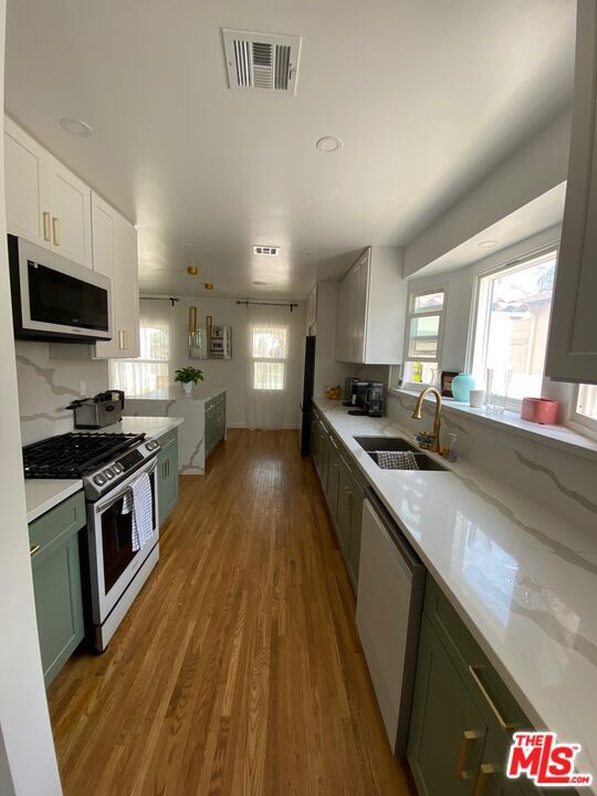 kitchen with stainless steel appliances, sink, green cabinetry, white cabinets, and light hardwood / wood-style floors