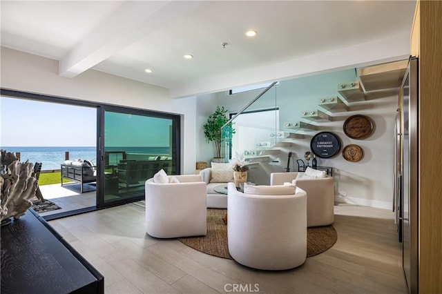 living room with beam ceiling, a water view, and light wood-type flooring