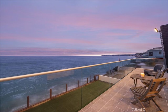 balcony at dusk featuring a water view