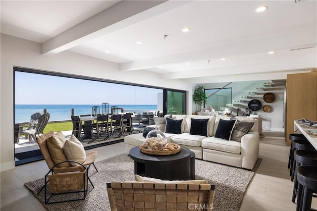 living room with beam ceiling, a water view, and light wood-type flooring