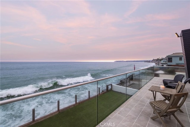 balcony at dusk featuring a water view