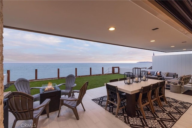 patio terrace at dusk with a yard, a water view, and an outdoor living space with a fire pit