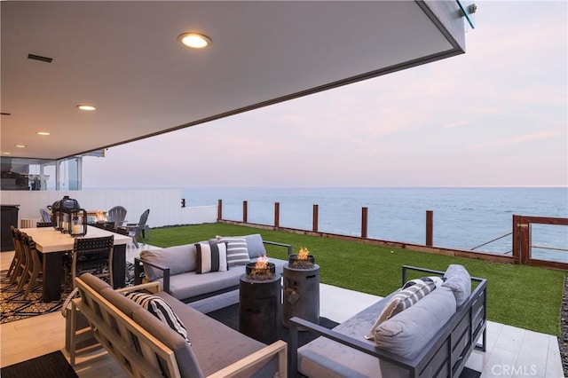 patio terrace at dusk featuring a lawn, a water view, and an outdoor hangout area