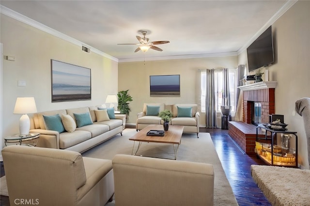 living room with a brick fireplace, crown molding, dark wood-type flooring, and ceiling fan