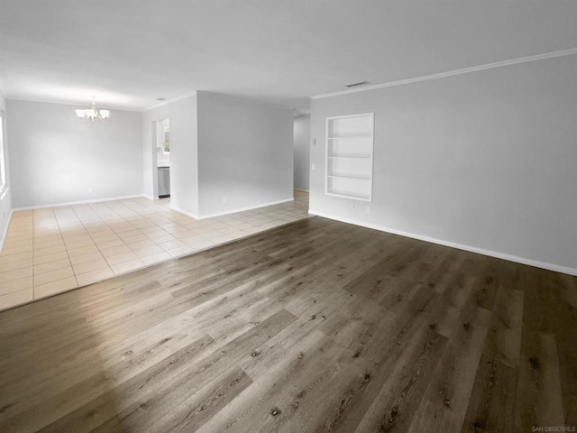 unfurnished room with an inviting chandelier, built in features, ornamental molding, and light hardwood / wood-style flooring