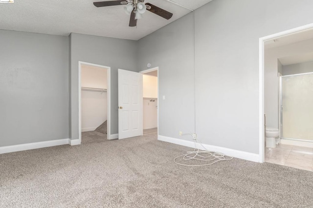 unfurnished bedroom with ceiling fan, ensuite bathroom, a walk in closet, and light carpet