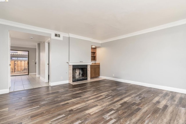 unfurnished living room with hardwood / wood-style flooring, ornamental molding, and a tiled fireplace