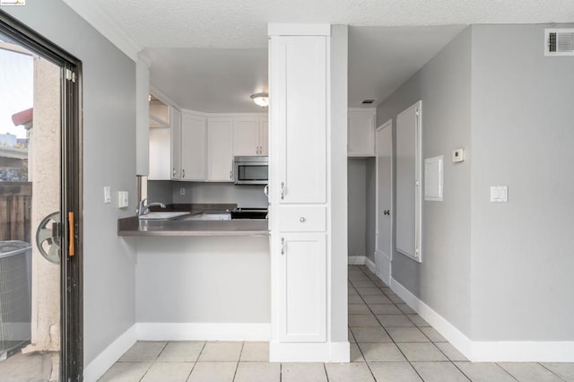 kitchen featuring a textured ceiling, sink, white cabinets, and light tile patterned floors