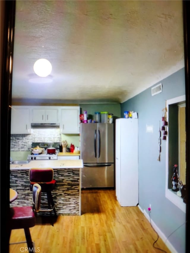 kitchen with white cabinets, tasteful backsplash, stainless steel refrigerator, white stove, and light hardwood / wood-style floors