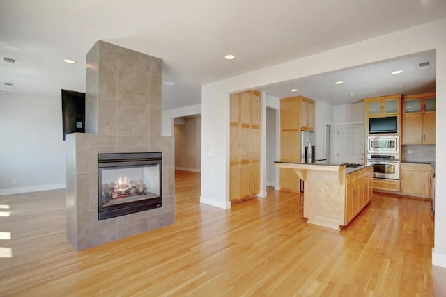 kitchen featuring a kitchen bar, appliances with stainless steel finishes, light hardwood / wood-style flooring, a tile fireplace, and a center island