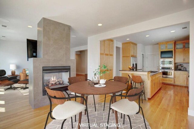 dining space with light wood-type flooring and a tiled fireplace