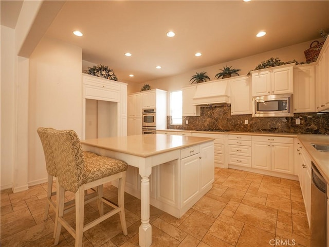 kitchen with custom exhaust hood, a center island, appliances with stainless steel finishes, tasteful backsplash, and white cabinetry