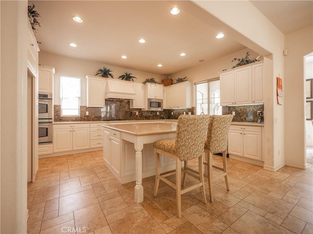 kitchen with a kitchen island, a kitchen bar, decorative backsplash, white cabinets, and appliances with stainless steel finishes