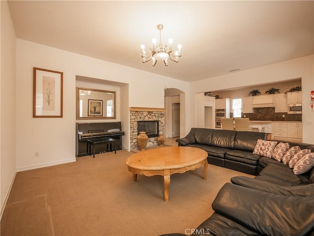 carpeted living room with a chandelier and a stone fireplace