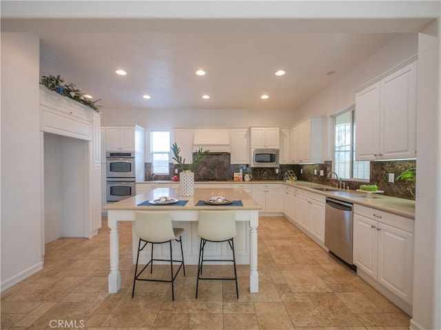 kitchen with sink, a breakfast bar area, appliances with stainless steel finishes, white cabinets, and a kitchen island