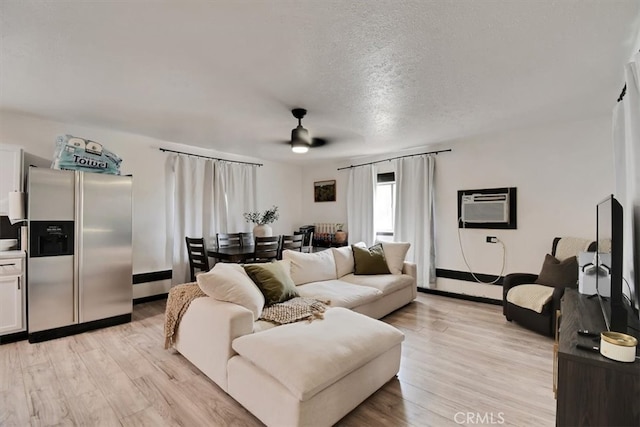 living room featuring ceiling fan, a wall mounted AC, a textured ceiling, and light wood-type flooring