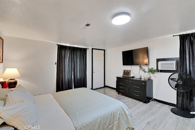 bedroom featuring light hardwood / wood-style floors, a textured ceiling, and a wall unit AC