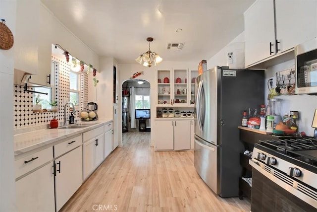 kitchen with white cabinets, light wood-type flooring, stainless steel appliances, decorative light fixtures, and sink