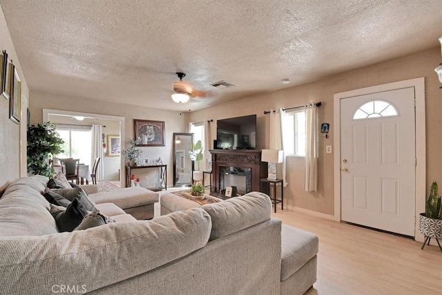 living room with light hardwood / wood-style floors, a textured ceiling, a wealth of natural light, and ceiling fan