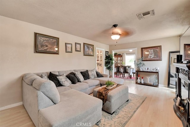 living room with light hardwood / wood-style flooring, a textured ceiling, and ceiling fan