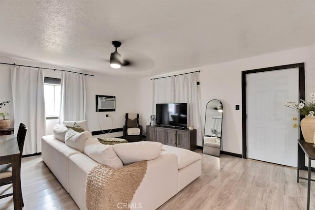 living room with a textured ceiling, an AC wall unit, light wood-type flooring, and ceiling fan