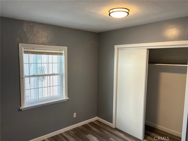 unfurnished bedroom featuring a textured ceiling, dark hardwood / wood-style floors, and a closet