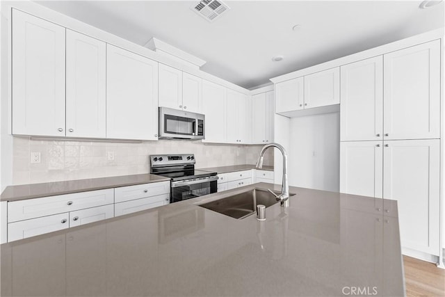 kitchen featuring sink, white cabinetry, stainless steel appliances, tasteful backsplash, and light hardwood / wood-style floors