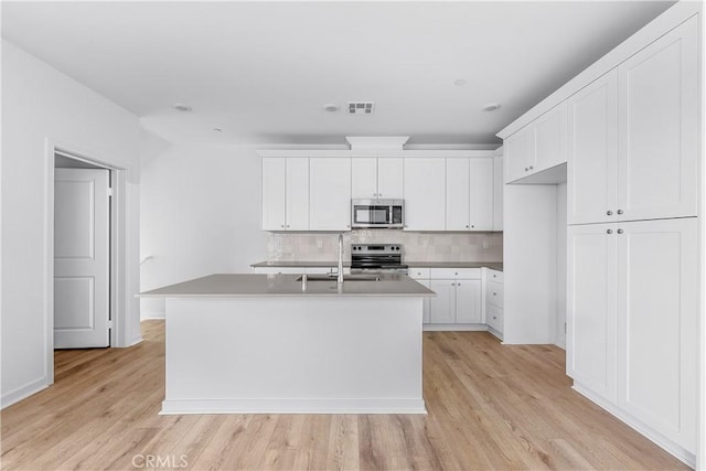 kitchen featuring sink, stainless steel appliances, white cabinets, a center island with sink, and light wood-type flooring