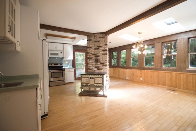 unfurnished living room featuring a skylight, sink, beamed ceiling, light hardwood / wood-style floors, and wood walls