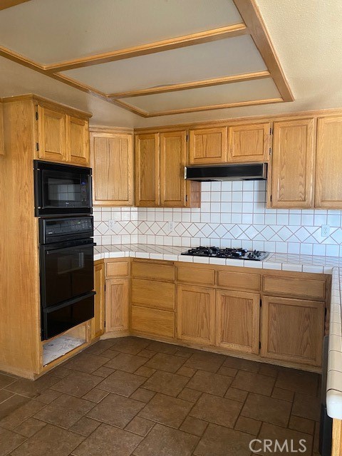 kitchen featuring light brown cabinetry, black appliances, tile countertops, and tasteful backsplash