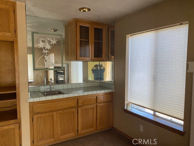 kitchen with dark tile patterned flooring, a textured ceiling, tile counters, and sink