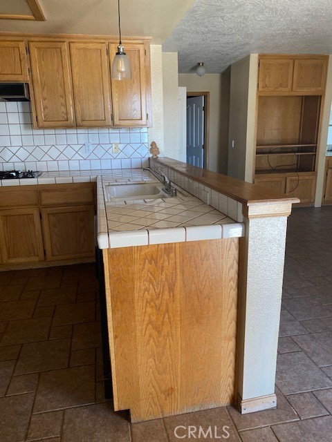 kitchen featuring tasteful backsplash, kitchen peninsula, decorative light fixtures, tile counters, and extractor fan