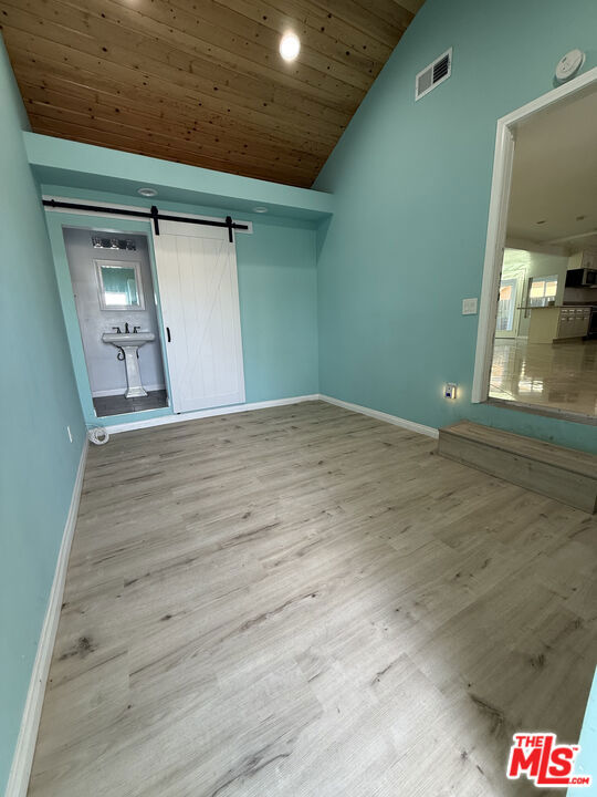 empty room featuring lofted ceiling, wooden ceiling, a barn door, and light wood-type flooring