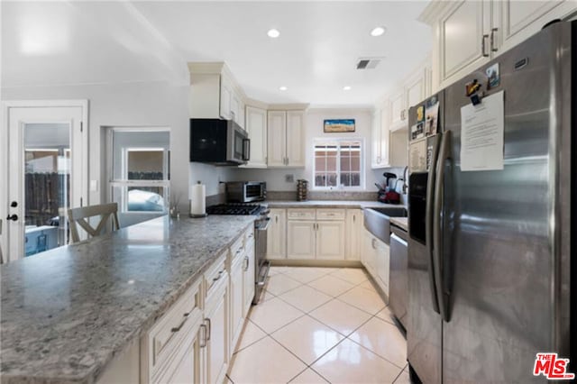 kitchen with appliances with stainless steel finishes, cream cabinets, sink, light tile patterned floors, and light stone countertops