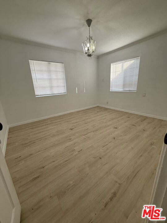 empty room with light hardwood / wood-style flooring, ornamental molding, and a chandelier