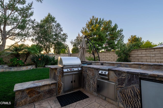 patio terrace at dusk with area for grilling and an outdoor kitchen