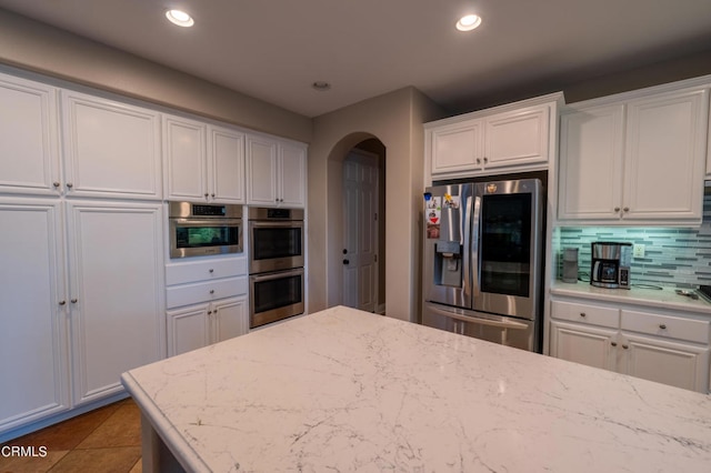 kitchen with tile patterned flooring, white cabinets, decorative backsplash, stainless steel appliances, and light stone countertops