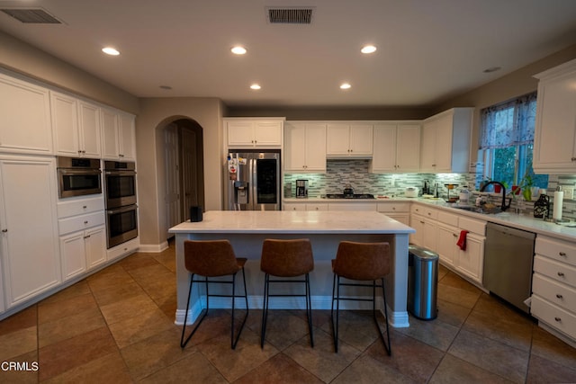 kitchen featuring a center island, sink, white cabinetry, stainless steel appliances, and backsplash