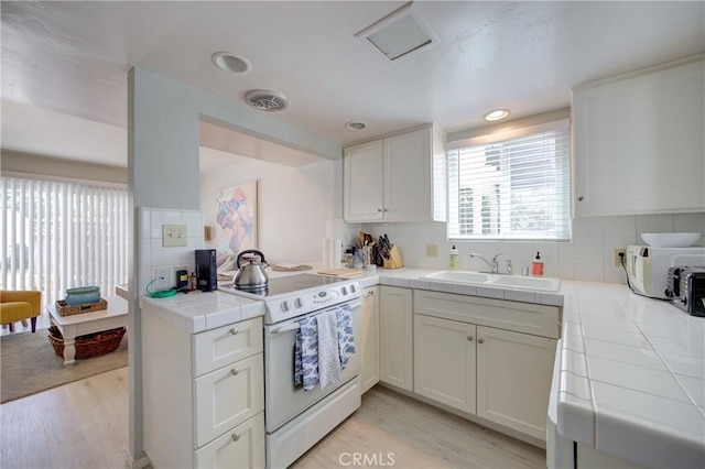 kitchen with tile countertops, white range with electric stovetop, sink, white cabinets, and decorative backsplash