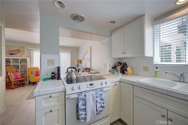 kitchen featuring sink, white range with electric cooktop, white cabinets, tile countertops, and kitchen peninsula