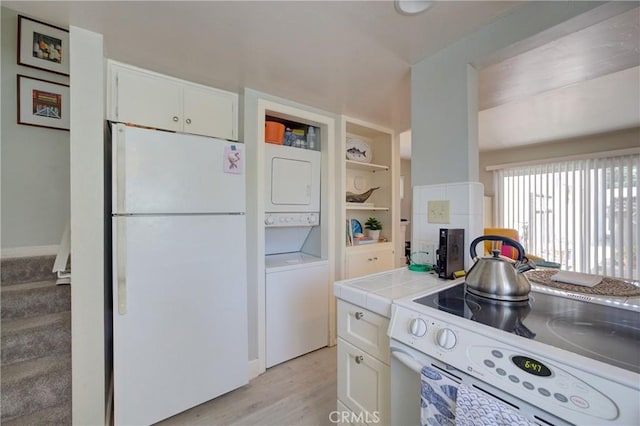 kitchen featuring white cabinetry, light wood-type flooring, stacked washer / drying machine, tile counters, and white appliances