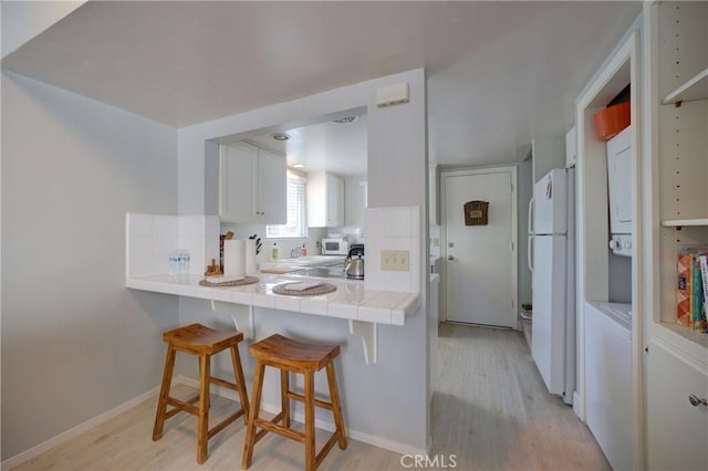 kitchen featuring a kitchen bar, light hardwood / wood-style flooring, tile counters, white appliances, and white cabinets