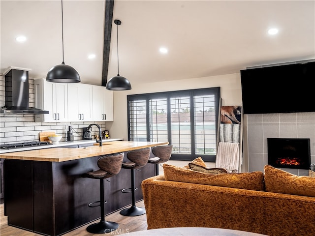 kitchen with hanging light fixtures, white cabinetry, stainless steel gas cooktop, wall chimney exhaust hood, and light hardwood / wood-style floors