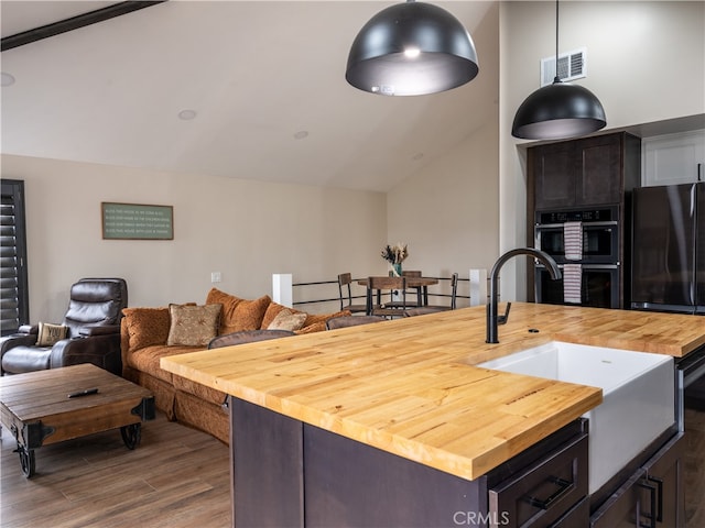 kitchen featuring stainless steel double oven, sink, vaulted ceiling, butcher block countertops, and dark hardwood / wood-style flooring