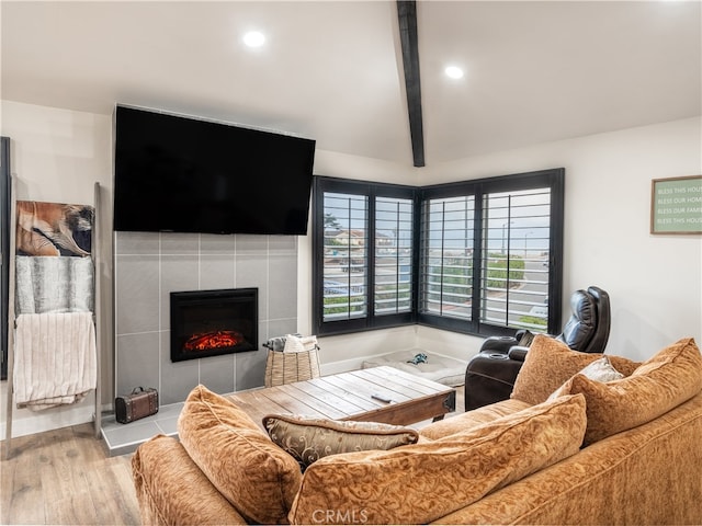 living room with vaulted ceiling with beams, light hardwood / wood-style flooring, and a tile fireplace