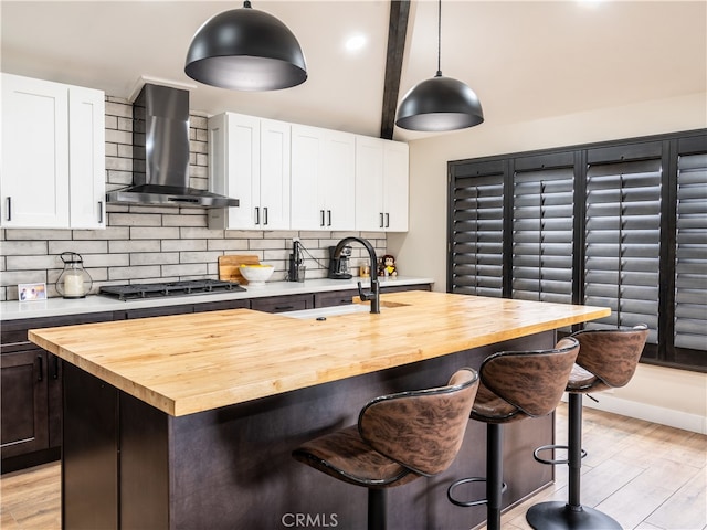 kitchen with stainless steel gas cooktop, wall chimney exhaust hood, butcher block countertops, and an island with sink